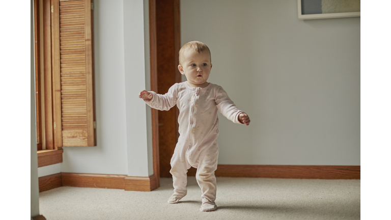 Baby first steps walking in bedroom with arms out with good balance