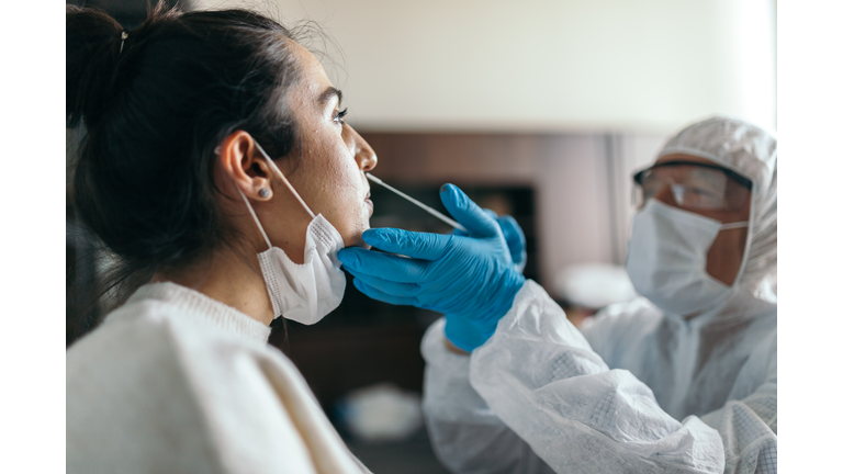 Doctor in protective workwear taking nose swab test from young woman