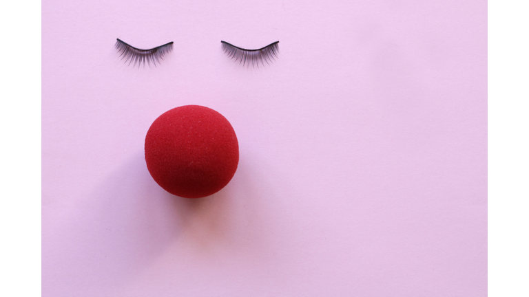 Face made with eyelashes and red nose on pink background