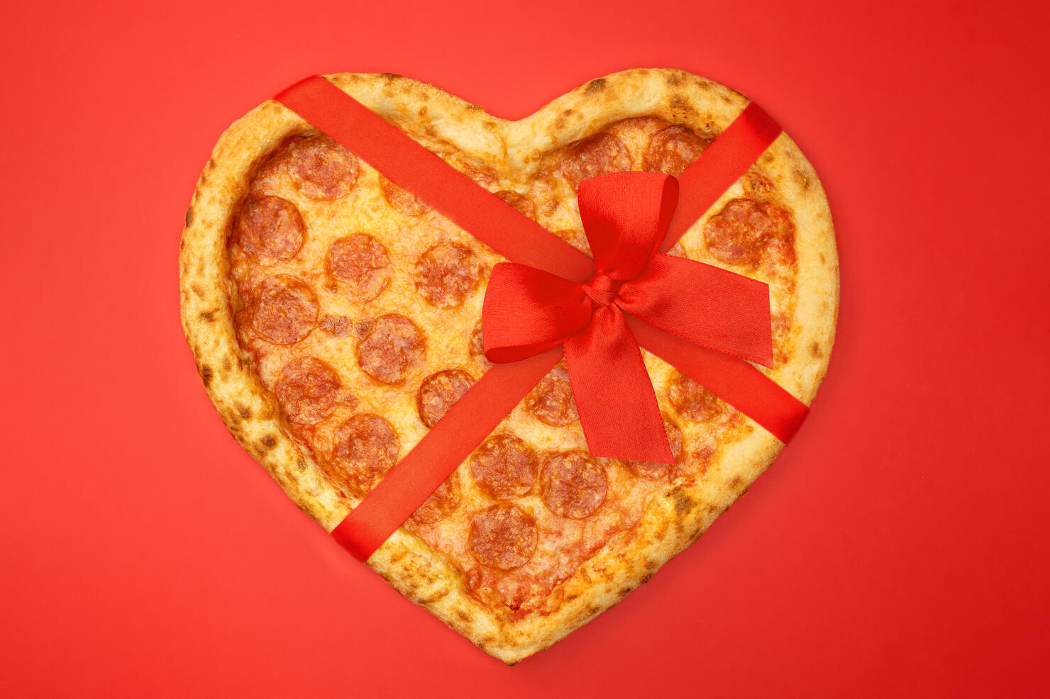 Pizza shaped heart with red bow ribbon for Valentine's Day romantic concept on red background