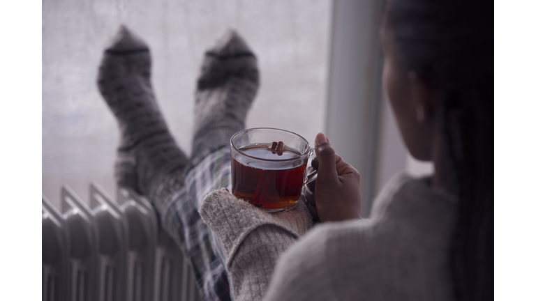 Over the shoulder image of a woman drinking tea at home in cold and wet weather.