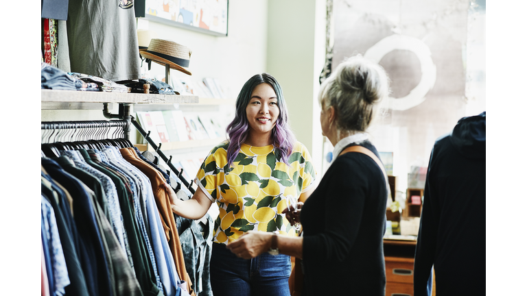 Smiling shopkeeper helping client shop in clothing boutique