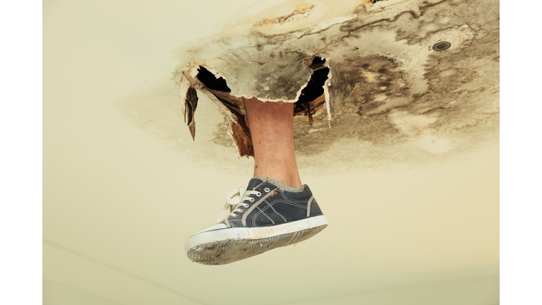 Foot in canvas shoe poking through rot in the ceiling