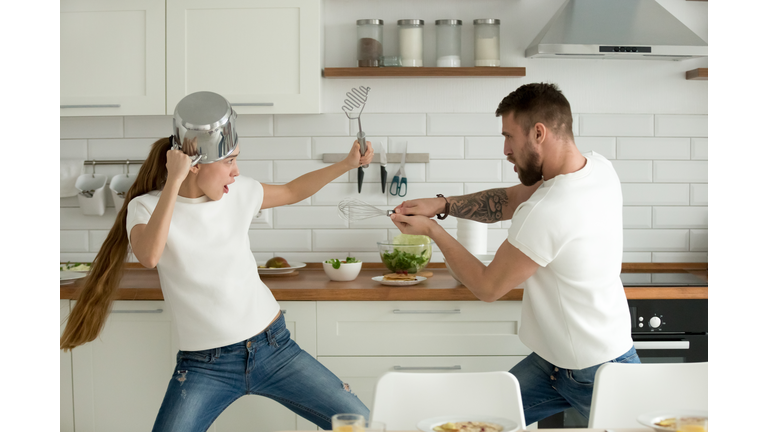 Funny couple having fun fighting with kitchen utensils cooking t