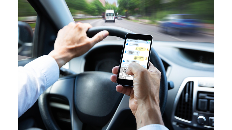 Man Typing Text Message On Mobile Phone While Driving Car