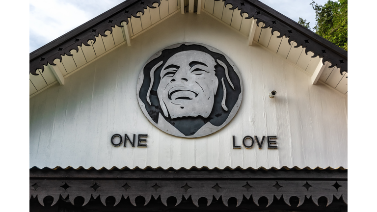 Nine Mile, Jamaica: One Love is written and Bob Marley\s portrait at entry house to the Bob Marley Mausoleum compound. Building is partially obscured by beautiful flowers