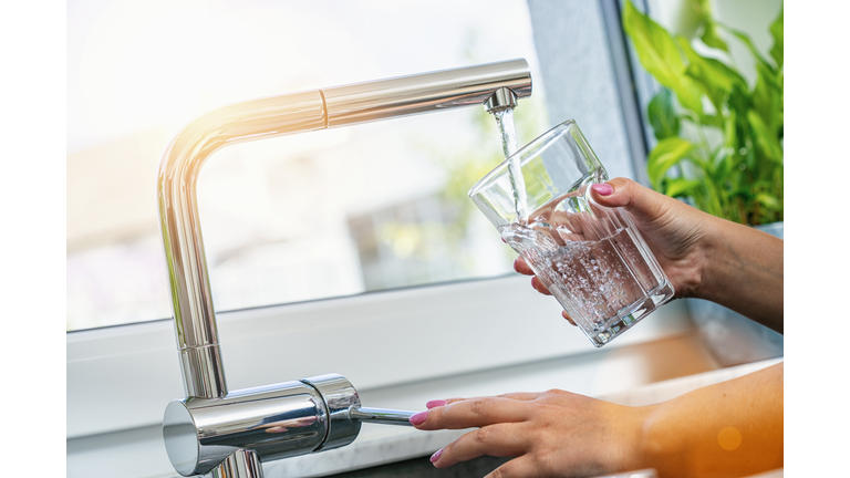 woman holding glass at water tap and filling water