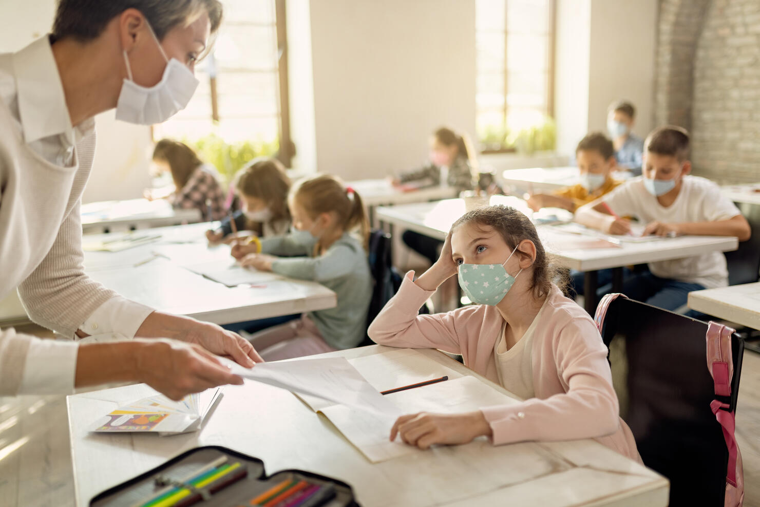 Schoolgirl with face mask talking to a teacher while receiving test results in the classroom.