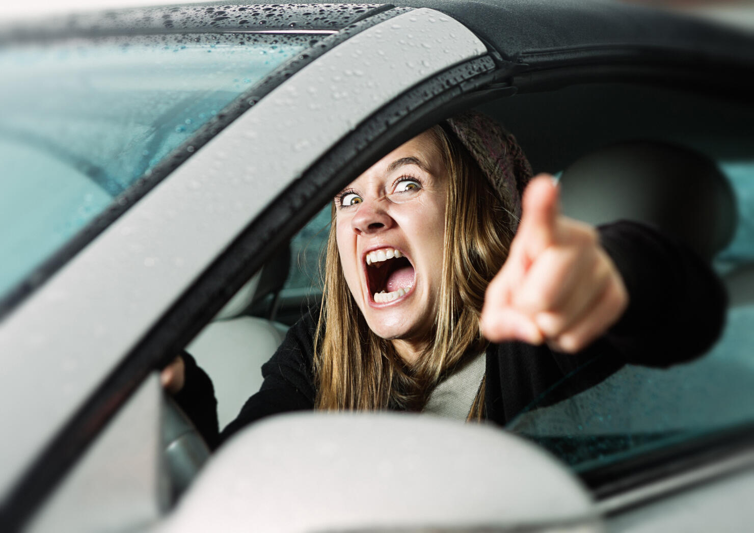Road rage! Enraged young woman driver shouts and points accusingly.