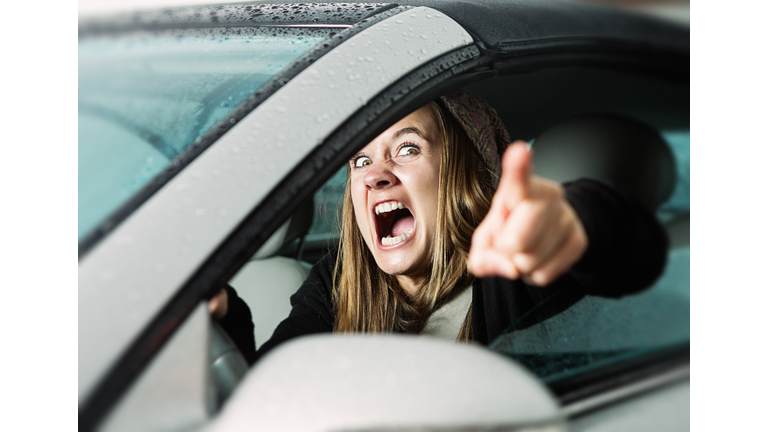 Road rage! Enraged young woman driver shouts and points accusingly.