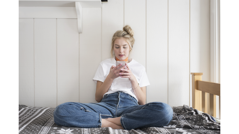 Teen girl with phone sitting on bed