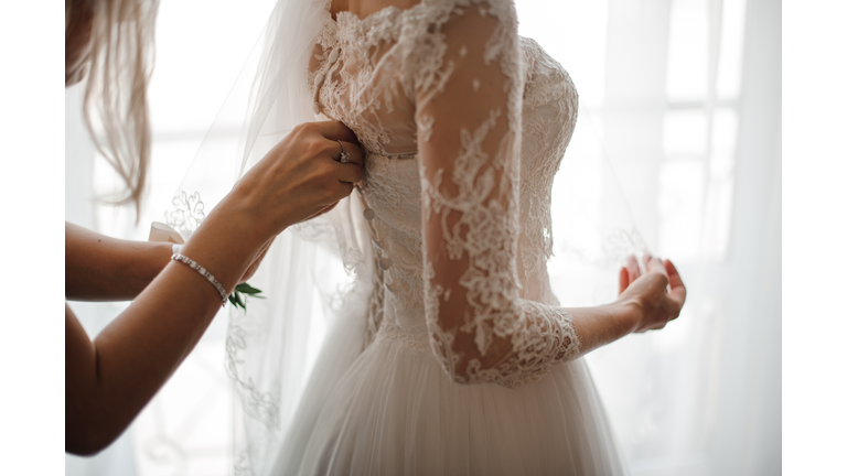 Bridesmaid making bow-knot on the back of brides wedding dress