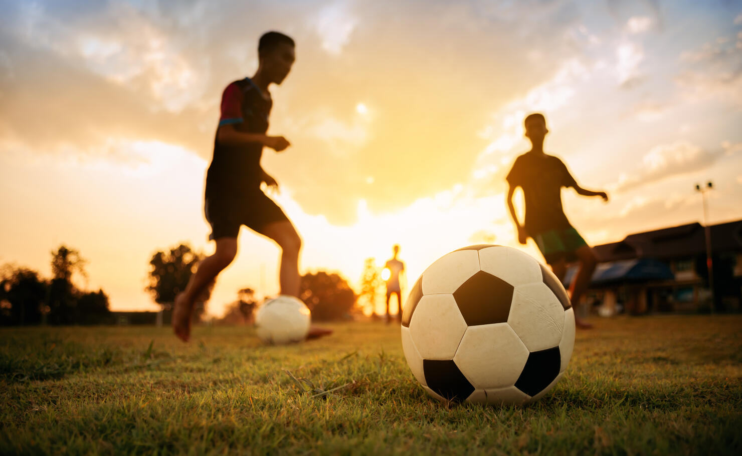 Silhouette action sport outdoors of a group of kids having fun playing soccer football for exercise in community rural area under the twilight sunset sky.