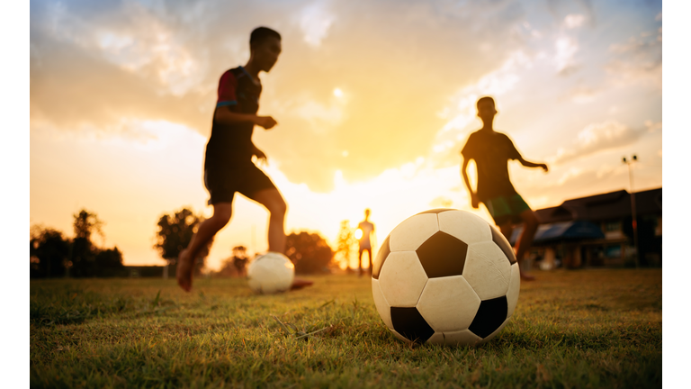 Silhouette action sport outdoors of a group of kids having fun playing soccer football for exercise in community rural area under the twilight sunset sky.