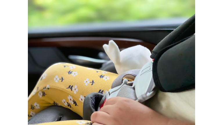 mixed-race toddler female clutches a toy rabbit while sleeping in car seat