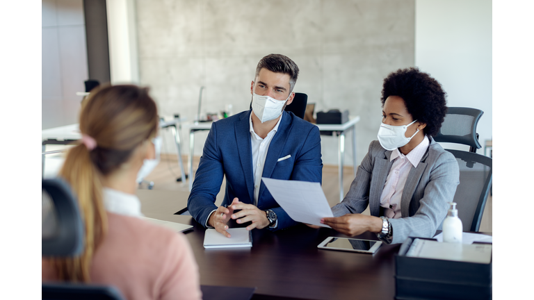Business coworkers wearing face masks while talking to potential job candidate in the office.