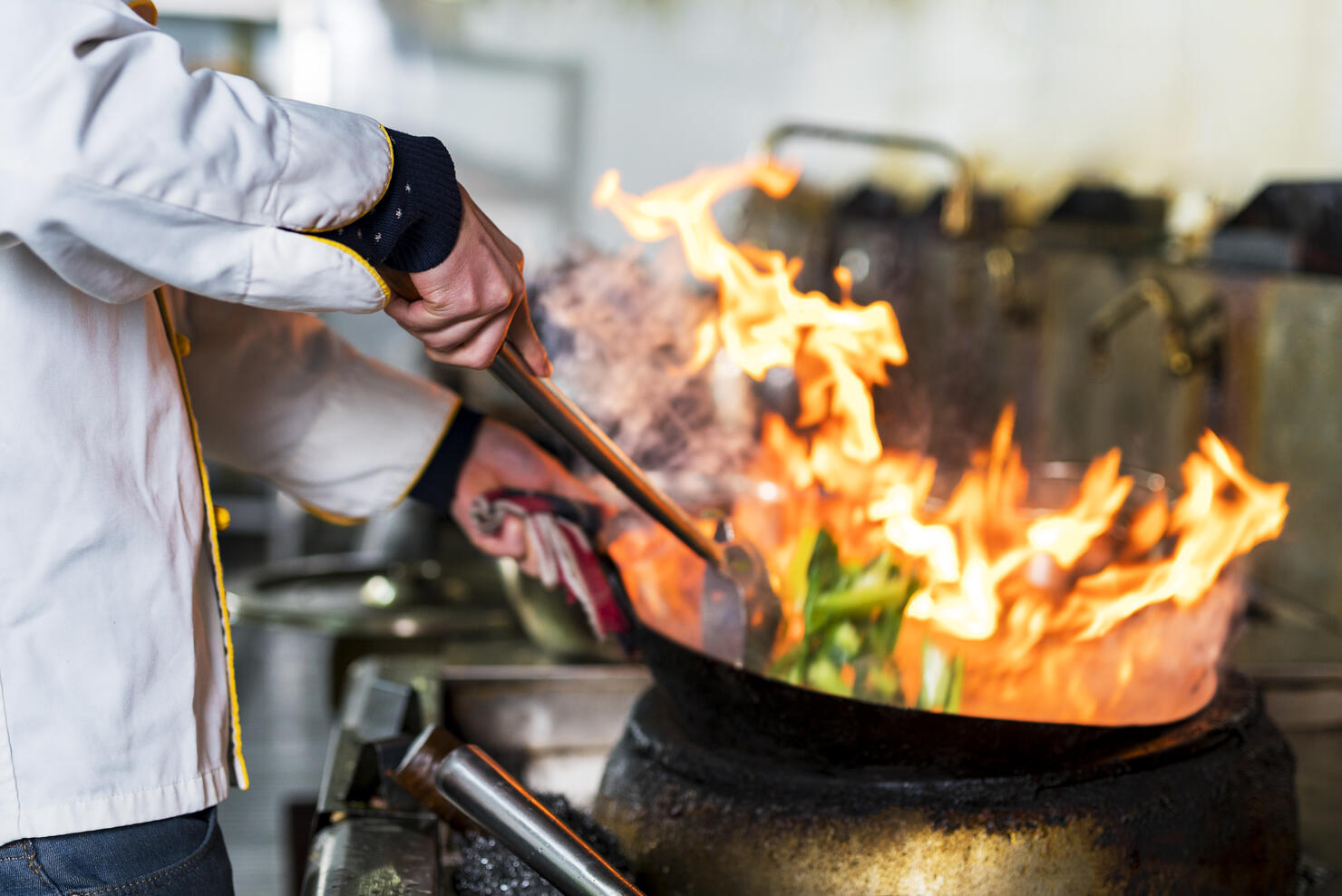 Chef cooking with flame in a frying pan on a kitchen stove