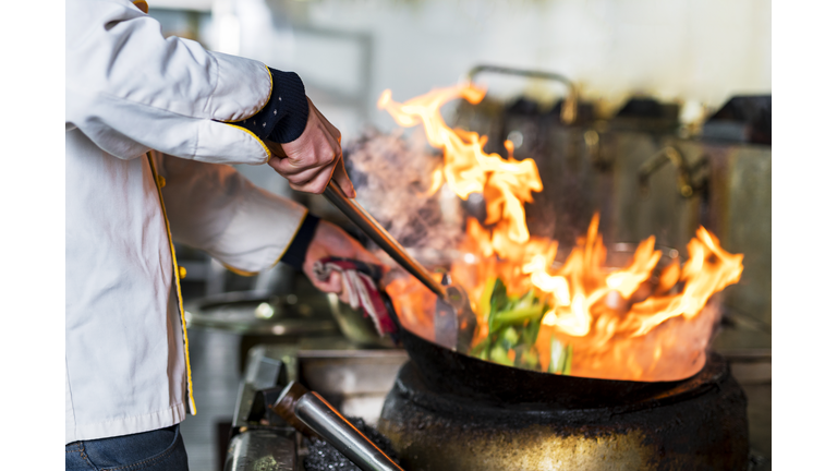 Chef cooking with flame in a frying pan on a kitchen stove