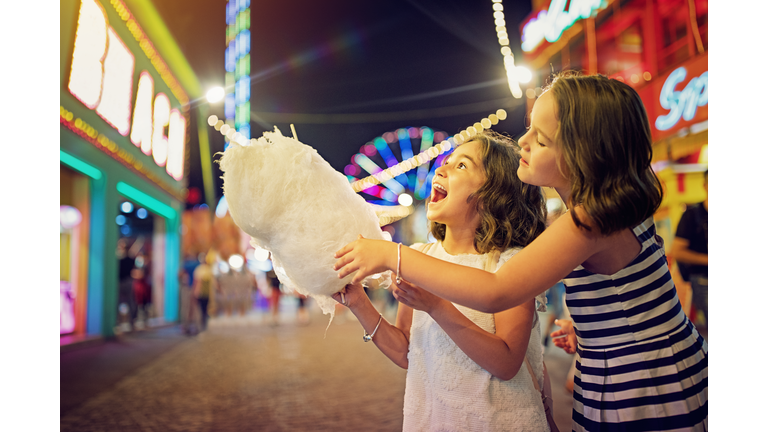 Two little girls are eating cotton candy at the fun fair and making fun