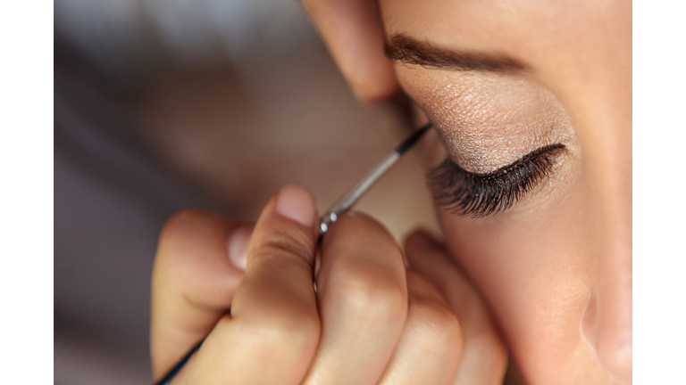 Beautiful fashion model applying makeup by makeup artist.