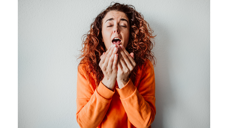 Woman Sneezing While Standing Against Wall