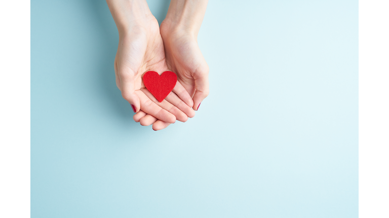 a person holding red heart in hands, donate and family insurance concept, on aquamarine background, copy space top view