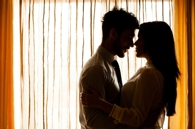 Man and woman about to kiss in front of window
