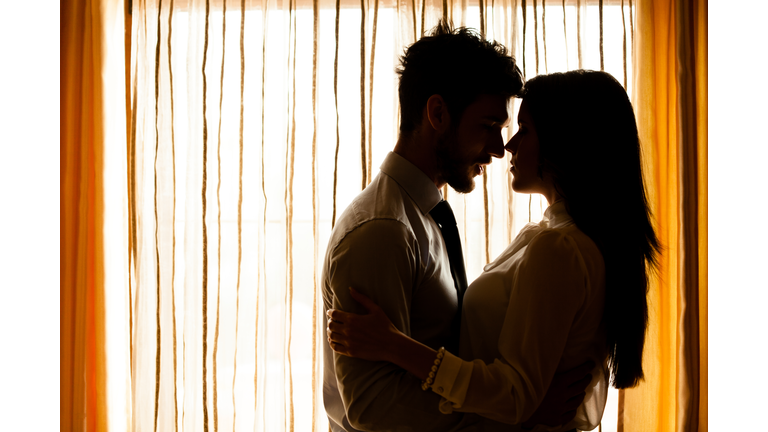 Man and woman about to kiss in front of window