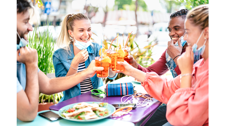 Friends drinking spritz at cocktail bar with face masks - New normal friendship concept with happy people having fun together toasting drinks at restaurant - Bright filter with focus on left woman