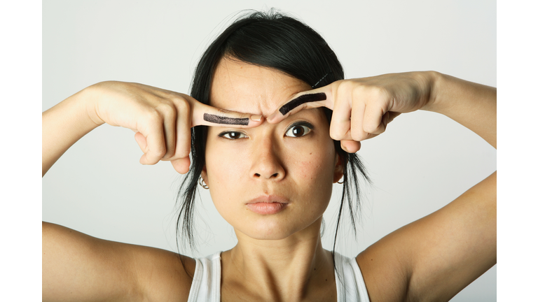 Young woman with fake eyebrows painted on fingers, portrait, close-up