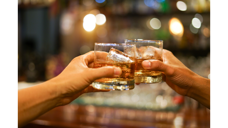 two men clinking glasses of whiskey drink alcohol beverage together at counter in the pub