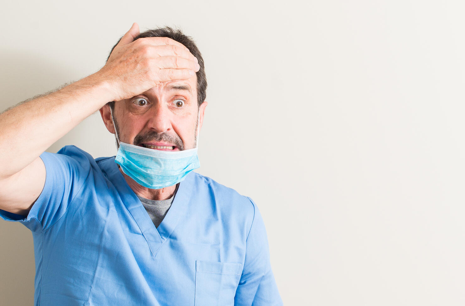 Senior doctor man using mask stressed with hand on head, shocked with shame and surprise face, angry and frustrated. Fear and upset for mistake.