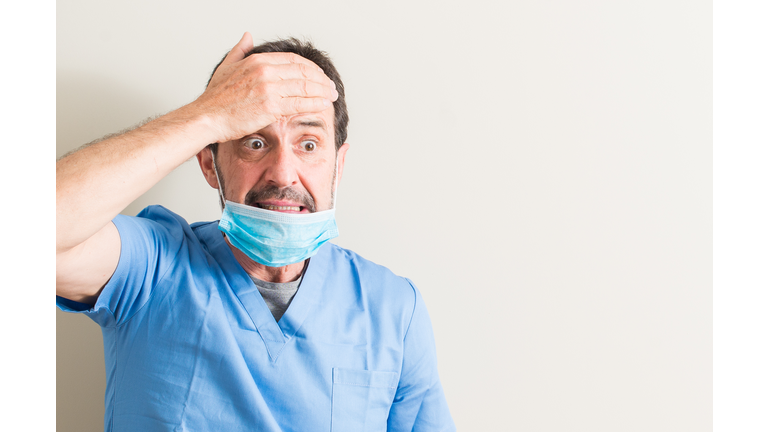 Senior doctor man using mask stressed with hand on head, shocked with shame and surprise face, angry and frustrated. Fear and upset for mistake.