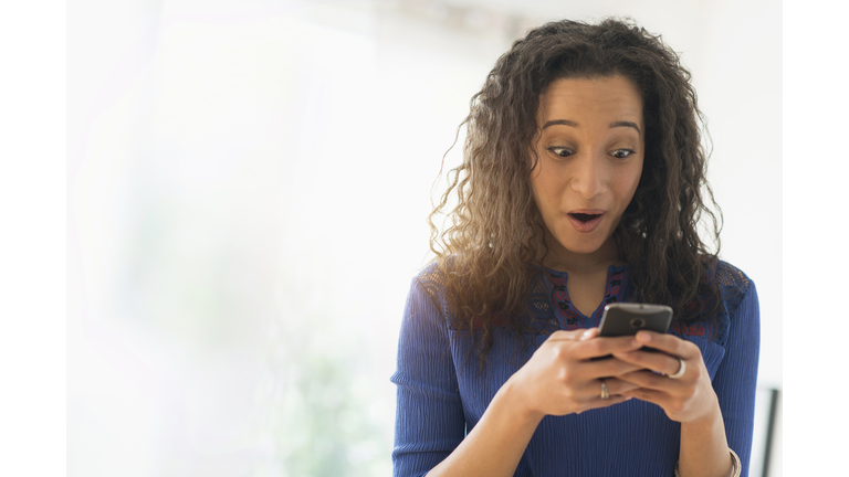 Close up of mixed race woman gasping at cell phone