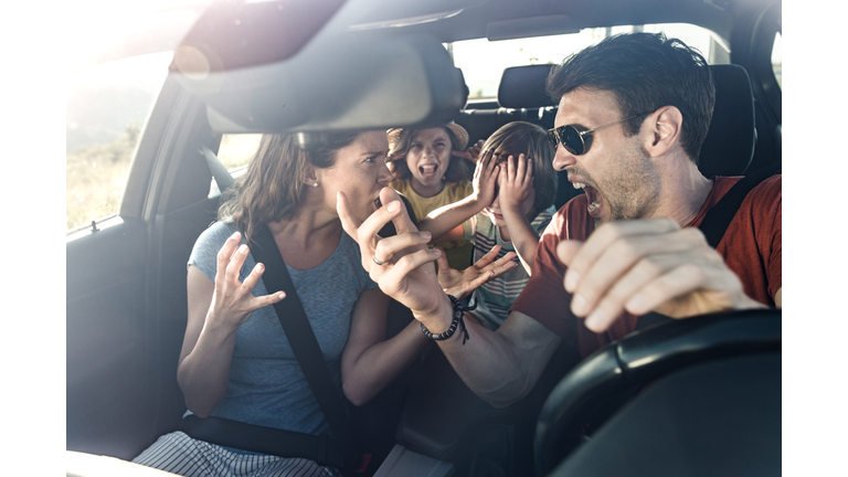 Frustrated parents arguing during trip by a car.