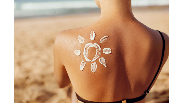 Skin care. Sun protection. Woman apply sun cream. Woman With Suntan Lotion On Beach In Form Of The Sun. Portrait Of Female With  Drawn Sun On A Shoulder. Suncream. Girl Holding Moisturizing Sunblock.