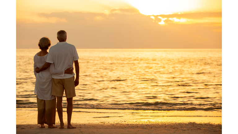 Senior man and woman couple embracing at sunset or sunrise on a deserted tropical beach