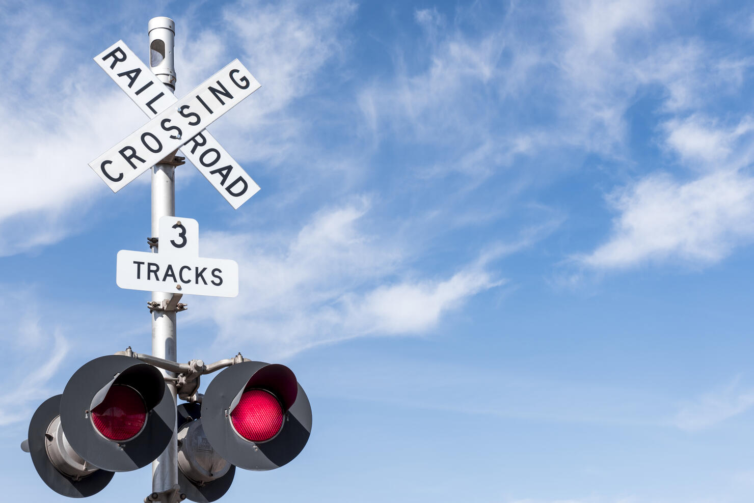 Railroad Crossing with Wispy Cloud in Blue Sky behind