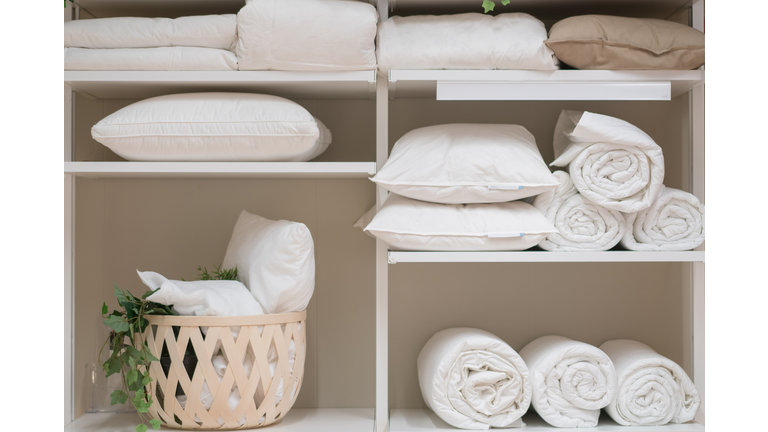 Various household items such as pillows and quilts standing in the white cupboard.