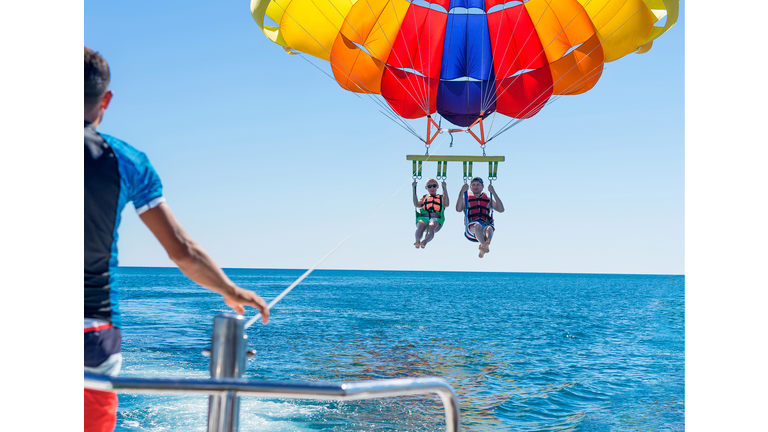 Happy couple Parasailing on Miami Beach in summer. Couple under parachute hanging mid air. Having fun. Tropical Paradise. Positive human emotions, feelings, family, travel, vacation.