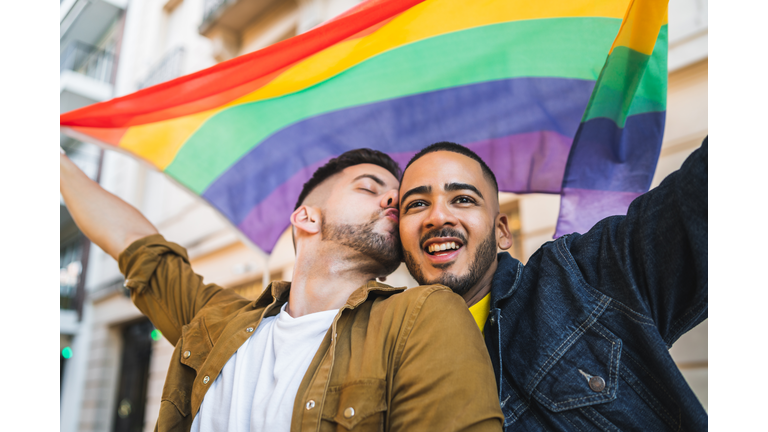 Gay Couple Holding Rainbow Flag While Standing In City