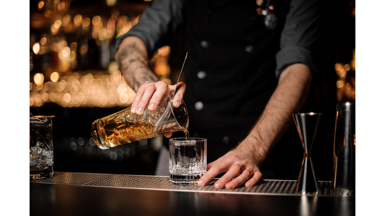Bartender pours cocktail adding whiskey in glass