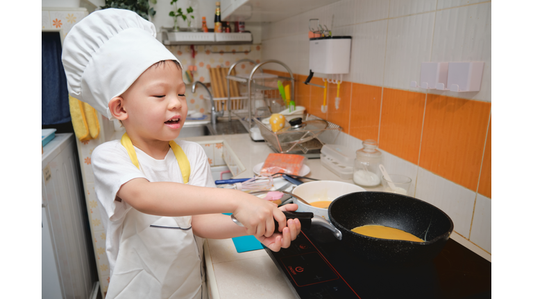 Cute happy Asian boy having fun cooking breakfast in kitchen, Fun indoor activities for kindergarten kids, Stay home Stay safe Have fun concept, photo in real life interior