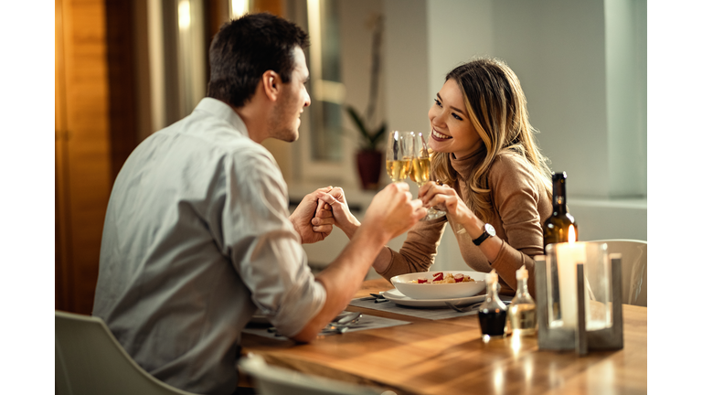 Happy couple toasting with Champagne during dinner at dining table.
