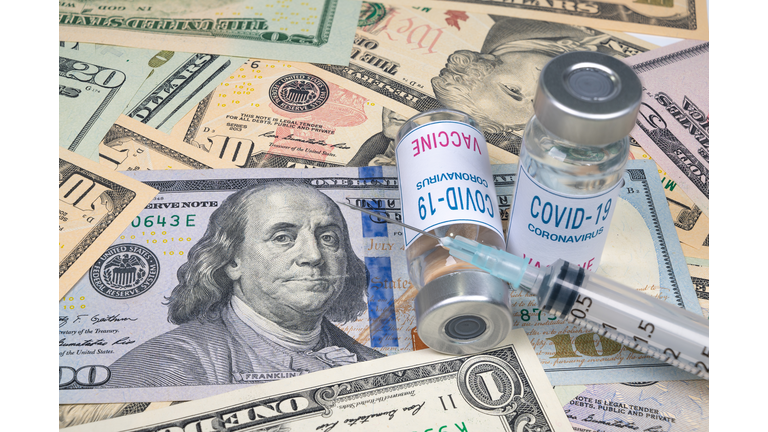 syringes and covid-19 vaccine ampoule lying on top of the US dollar.