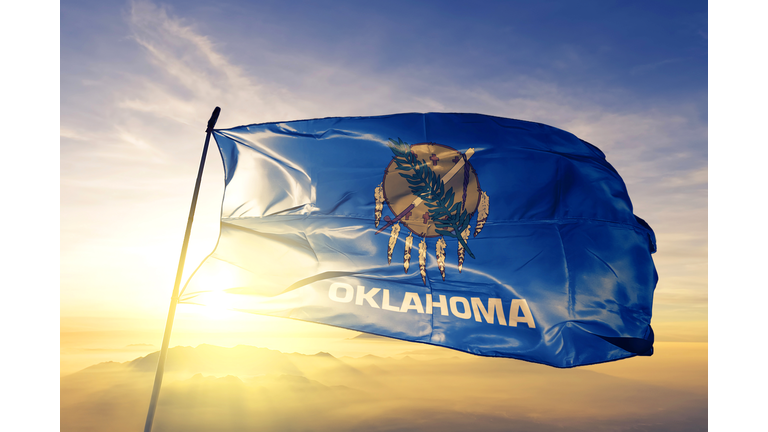 Oklahoma state of United States flag textile cloth fabric waving on the top sunrise mist fog