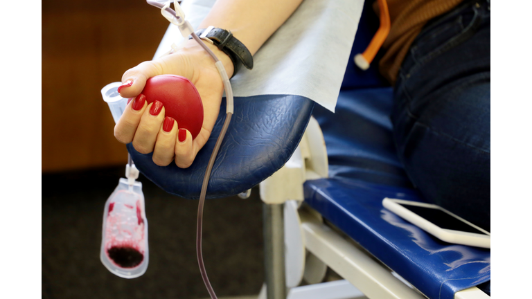 Woman blood donor in chair during donation with a blood bag and red bouncy ball in hand
