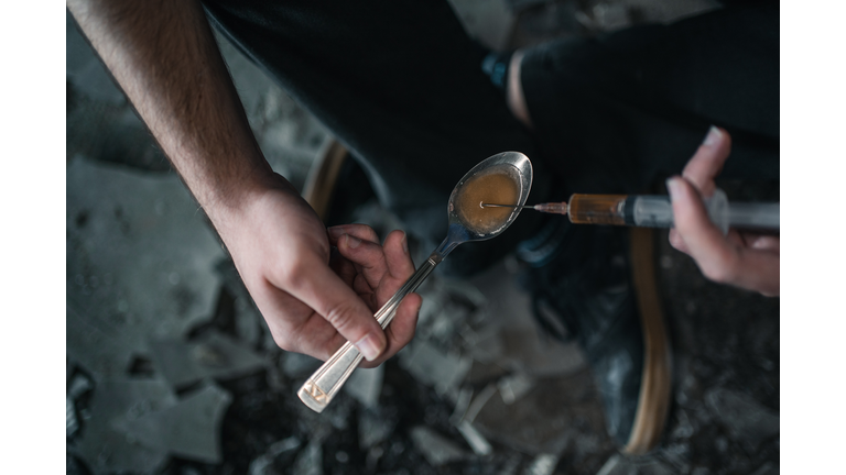 Drug addict using syringe preparing drug in spoon for shooting up