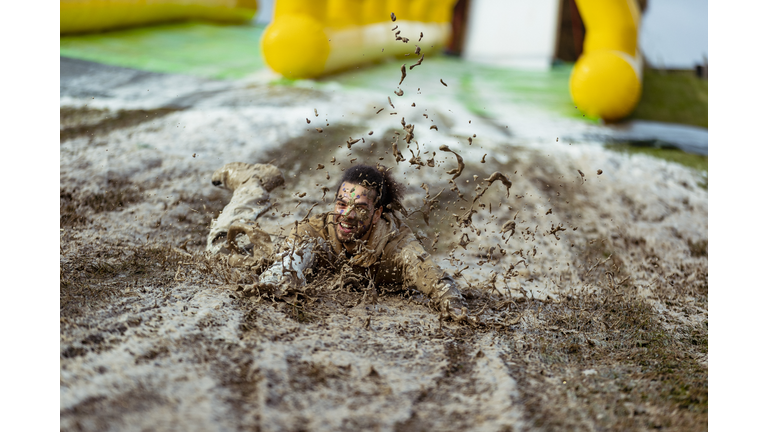 Man splashing head first on muddy slip and slide