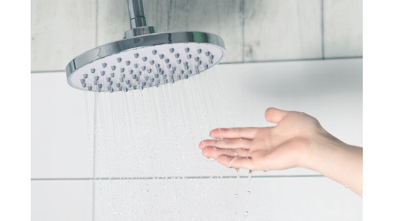 Female hand touching water pouring from a rain shower head, checking water temperature